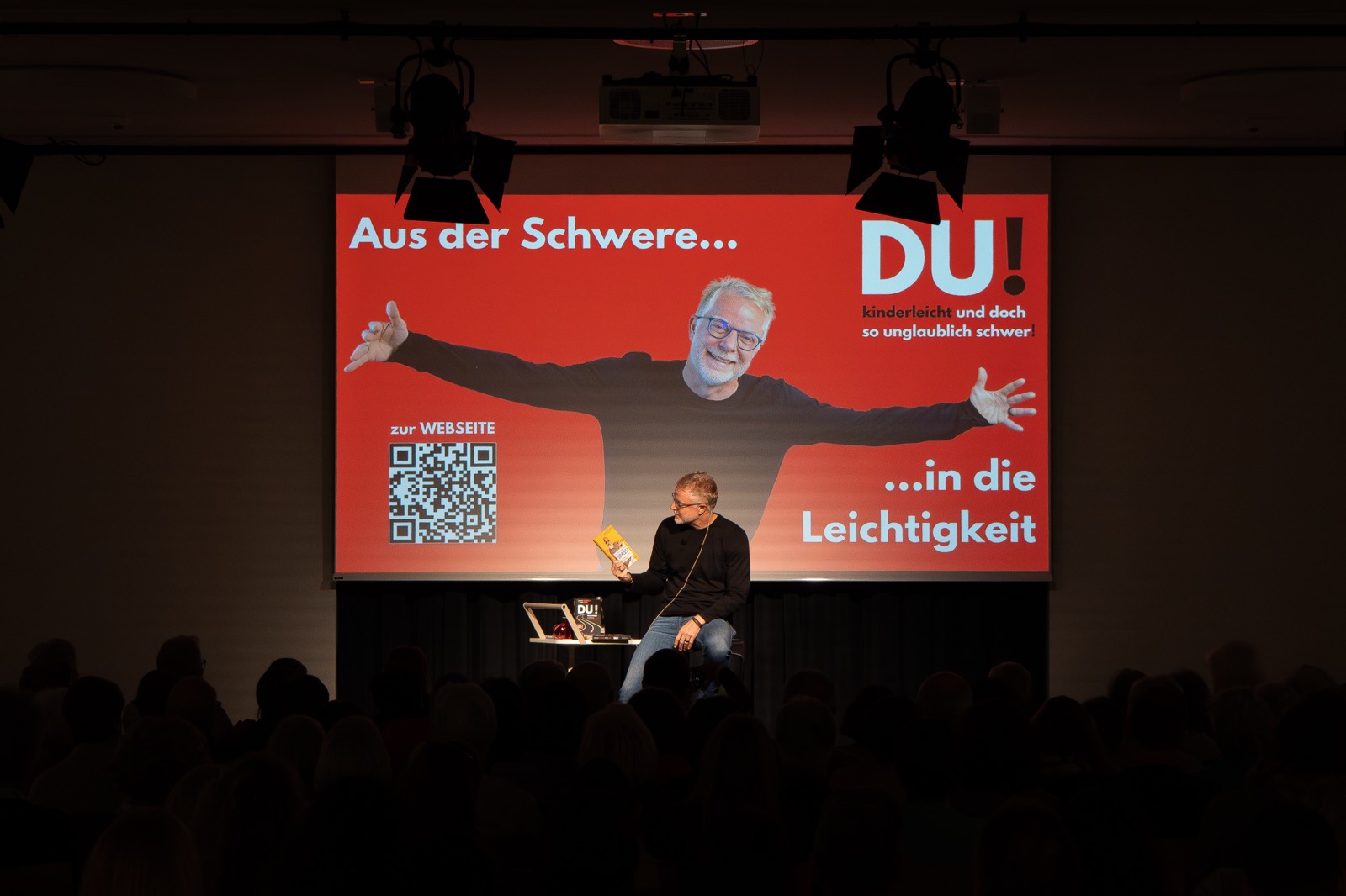 Redner auf dem Barhocker vor der großen Leinwand im abgedunkelten Saal