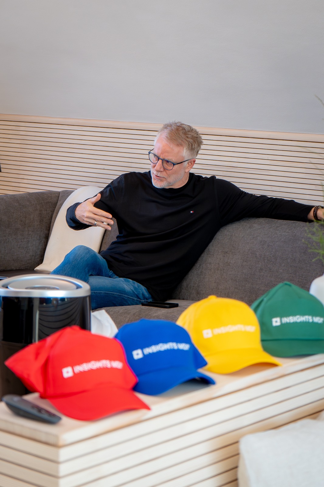 Trainer lehnt entspannt auf dem Sofa, davor bunte Caps