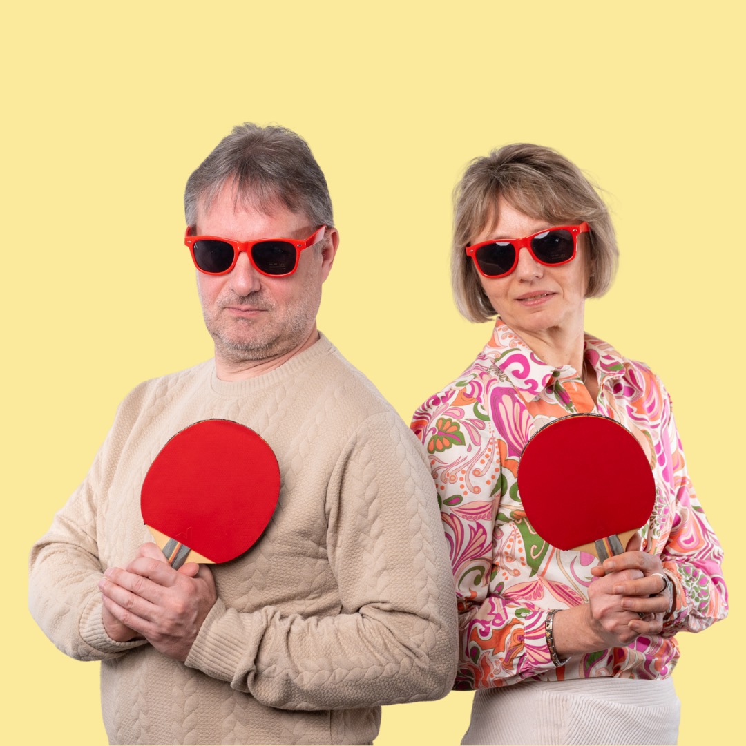 Duo mit Sonnenbrillen und Tischtennisschlägern vor gelbem Hintergrund