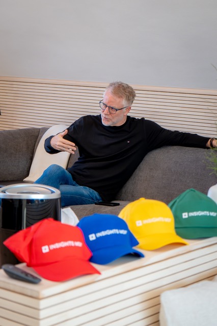 Trainer lehnt entspannt auf dem Sofa, davor bunte Caps