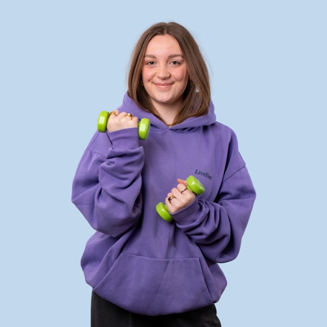Frau im lila Hoodie mit grünen Kurzhanteln