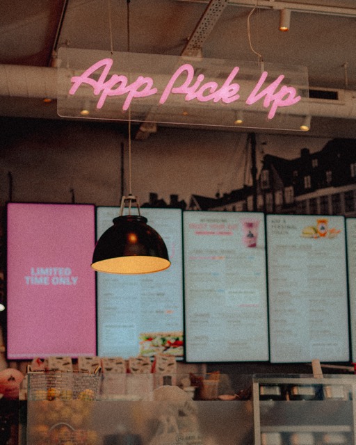 Neonschrift „App Pick Up“ über einer Theke